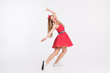 Young woman in red polka dot dress dancing against white background, evoking retro charm and lively...