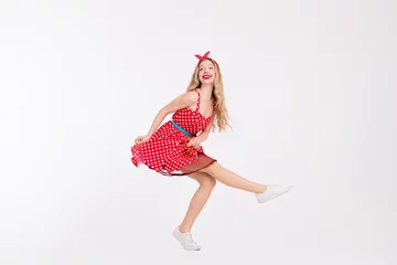 Fotobehang Smiling young woman in vintage red polka dot dress posing playfully on white background with stylish pinup look © deagreez