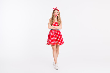 Young woman in retro red polka dot dress, wavy blonde hair, and headband posing stylishly on white background, evoking vintage charm