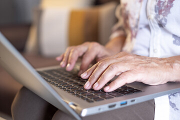 Close up view of woman hands typing on keyboard of laptop holding laptop on his knees