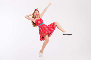 Fototapeta na wymiar Joyful young woman in a nostalgic red polka dot dress dancing energetically against a white backdrop, celebrating retro style