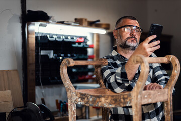 Portait of carpenter looking at his mobile phone in his workshop.