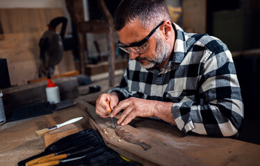 Carpenter sitting in his workshop restoring old piece of furniture with carving tool.
