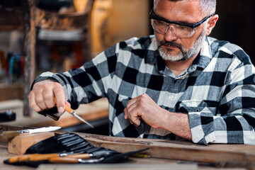 Carpenter sitting in his workshop restoring old piece of furniture with carving tool.