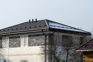 Construction Concept: A partially constructed house with dark roof tiles and some snow, unfinished walls and wrapped windows.