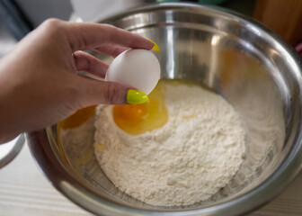 woman's hand holding an egg over a metal mixing bowl filled with flour