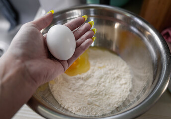 woman's hand holding an egg in the palm of a hand over a metal mixing bowl filled with flour