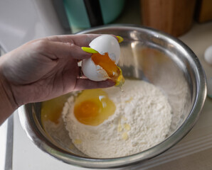 woman's hand cracking an egg over a metal mixing bowl filled with flour
