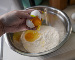 woman's hand cracking an egg over a mixing bowl filled with flour