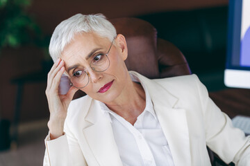 Businesswoman with a thoughtful expression sitting in her office chair dressed in formal white...