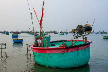 Traditional round Vietnamese basket boat floating in a crowded harbor with colorful fishing boats