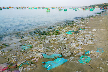 Plastic waste scattered along the beach with anchored fishing boats, polluted Vietnamese seashore