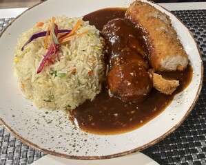 A plate of fried rice, Breaded chicken rolls stuffed with button mushrooms, capsicum, and carrots topped with a spicy-sweet and sour sauce.