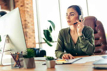 Young businesswoman in a modern office environment using a headset and computer while focusing on her professional tasks
