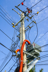 Tangled overhead electrical wires on a power pole under blue sky in a tropical Southeast Asian town