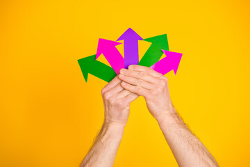 Hands holding colorful arrows pointing in various directions on a vibrant yellow background, symbolizing choice and decision-making