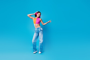Cheerful young woman in vibrant attire listening to music with headphones on a colorful background expressing happiness