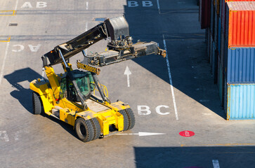 Yellow Reach Stacker Moving Between Shipping Containers in Cargo Terminal