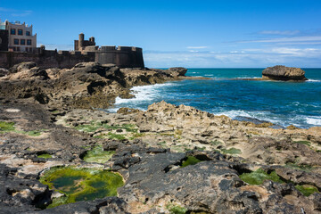 View of Rempart Mogador, an 18th-century fortress on the rocky Atlantic coast in the old medina of Essaouira, Morocco. Historic fortification by the sea under a clear blue sky