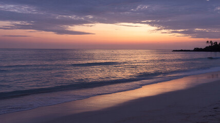 Serene coastal scene captured during sunset with beach, ocean, and pastel sky.