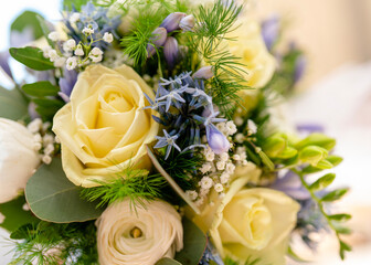 Lovely floral arrangement featuring light yellow roses and blue flowers set in a bright indoor...