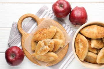 Delicious fried pyrizhky (stuffed pies) and apples on white wooden table, flat lay