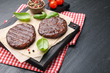 Delicious hamburger patties, tomatoes and spices on black table, closeup. Space for text