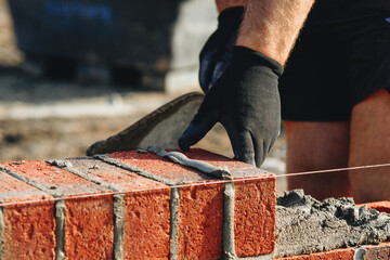 Close-up of skilled bricklayer working on construction site laying red bricks for wall construction...