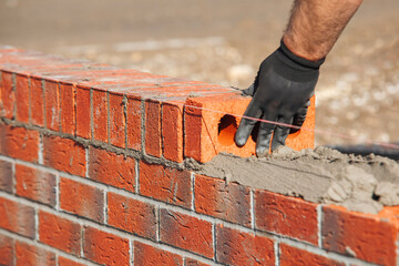 Close-up of skilled bricklayer working on construction site laying red bricks for wall construction...