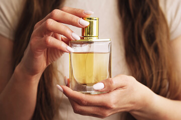 Woman holding perfume bottle. Golden cap and elegant hands. Close-up shot of fragrance. Long brown...