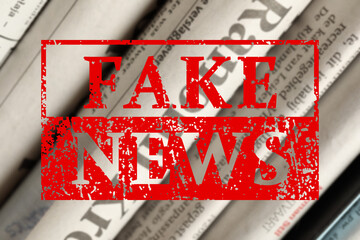Red Fake News stamp and newspapers in different languages as background, closeup