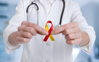 World Hepatitis Day. Doctor with yellow-red awareness ribbon on blurred background, closeup