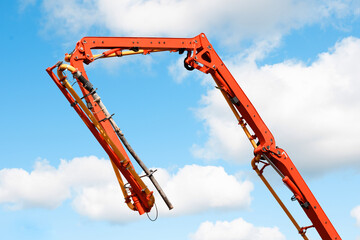 Construction machine mobile concrete pump with red extended boom arms against blue sky and  clouds preparing for pour