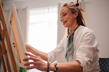 Female artist placing canvas on easel, preparing to paint in art studio