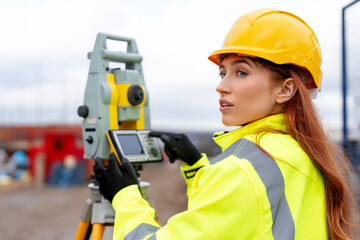 Portrait of young female Surveyor using a total station for land measurement at construction site showcasing safety gear and professional focus
