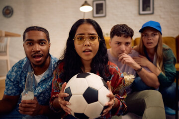 Multiracial group of disappointed soccer fans watching match on TV at home.