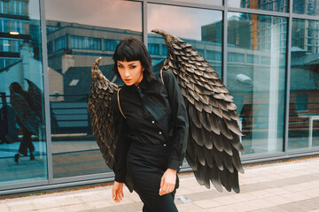 Unique urban fashion featuring model with large decorative wings while posing outside a modern...