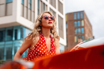 Woman in a red polka dot dress and sunglasses enjoy a stylish moment in an urban city setting...