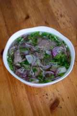 Pho bo vietnamese traditional spicy hot soup served in deep white bowl on wooden table with beef meat and onion coriander herbs