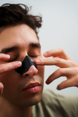 Young guy applying charcoal nose strip for deep nose pores cleaning. Male beauty and skincare...