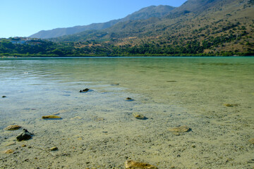 Clear turquoise waters of Lake Kournas with mountainous landscape under blue sky in Crete, Greece