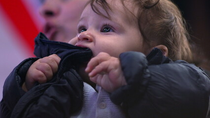 Baby chewing on jacket, close-up view, curious expression, wearing winter coat, everyday family...