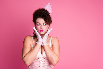 A young woman in a vintage corset looks playful against a pink background, embodying elegance with...