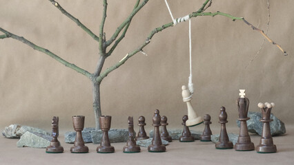 chess piece white bishop hanging on noose among black chess pieces