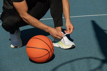 Close up basketball player tying sports shoes in basketball court outdoors. Last preparation. Team...