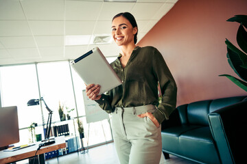 Confident businesswoman standing in modern office holding a tablet, dressed in stylish attire,...
