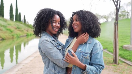 African two happy twin sisters are embracing and touching their curly afro hair, enjoying a sunny day together in a park - Powered by Adobe