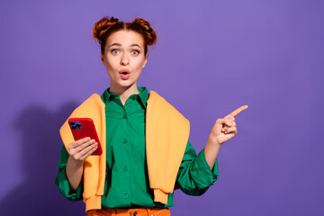 Cheerful red haired woman holding a smartphone while gesturing amazedly, standing against a vibrant...