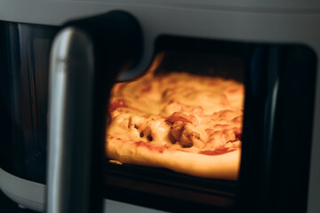 A close up of a pizza being baked in an air fryer showing the melted cheese and toppings with warm...