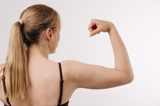 Strong woman flexing her bicep, showcasing physical fitness and empowerment, with a neutral background emphasizing her muscular definition and determination in an action pose of strength confidence